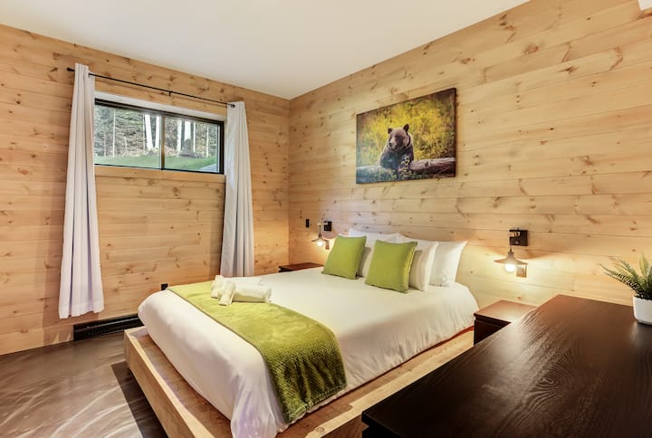Habitación amplia de madera natural, cama grande y toques de color verde. Tranquilidad absoluta.