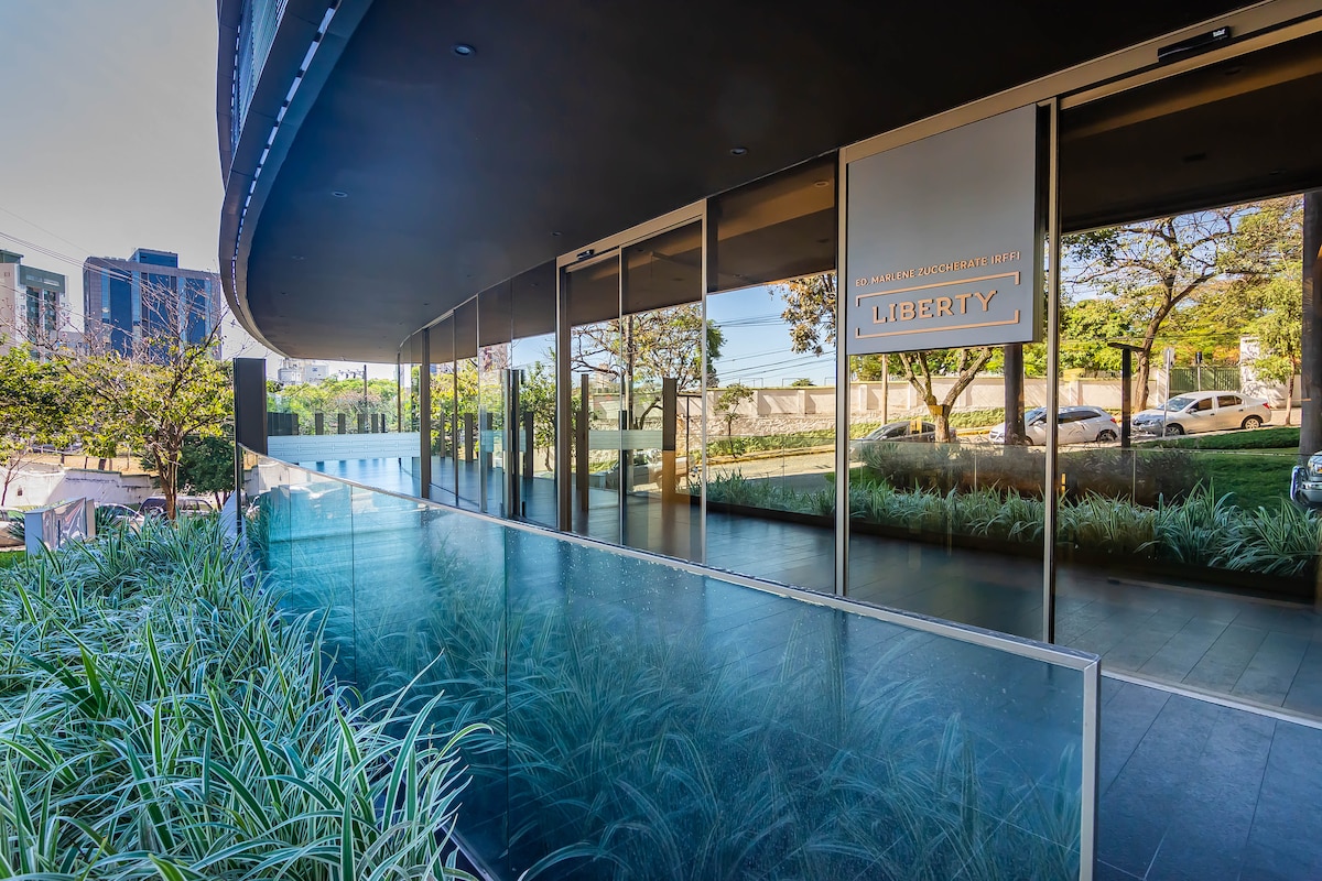 An inviting entryway features sleek glass panels and modern architecture, surrounded by well-maintained greenery. The pathway leads to the main entrance, marked by a sign labeled 'LIBERTY.' Natural light enhances the contemporary design, creating a warm and open atmosphere.