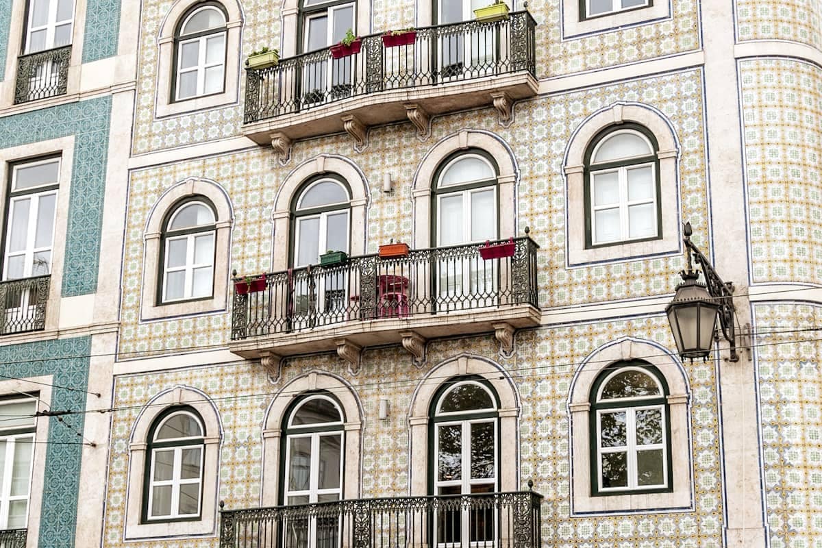 The building's facade displays a harmonious blend of original tiles and architectural details. Multiple balconies are visible, each adorned with colorful planters and garments, inviting a sense of local charm and history. Large windows allow for ample natural light, enhancing the building's elegant presence.