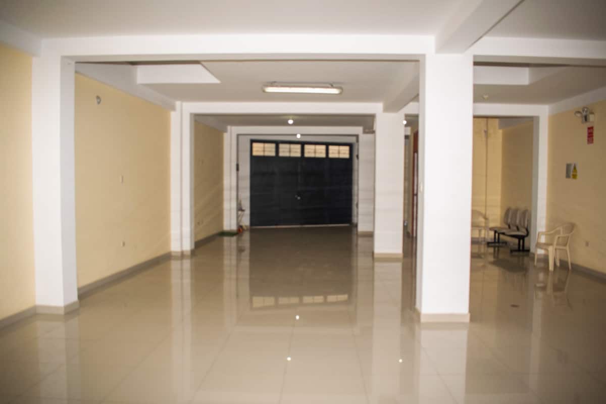 A spacious area is depicted with smooth, glossy flooring. The walls are painted in a soft yellow hue, and three white chairs are placed against one wall. A large garage door is visible, contributing to the open atmosphere.