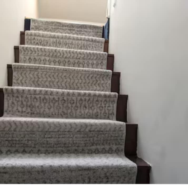 Sturdy wooden stairs are carpeted with a patterned runner, leading upward. The walls are painted a soft color, emphasizing the clean and simple design of this access route.