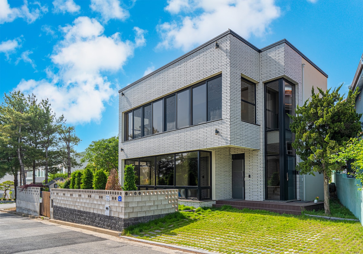 The modern two-story building features a sleek facade with large glass windows. Surrounding greenery adds to the inviting appearance. A spacious entrance is visible, while the outdoor area includes manicured shrubs and a clean pathway, enhancing the property's appeal.