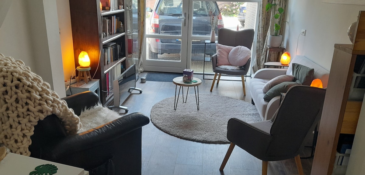 A cozy living area features a mix of seating options, including a small sofa and comfortable chairs. A round coffee table sits at the center, with ambient lighting provided by two soft-glow lamps. A plush rug covers the floor, adding comfort to the space.