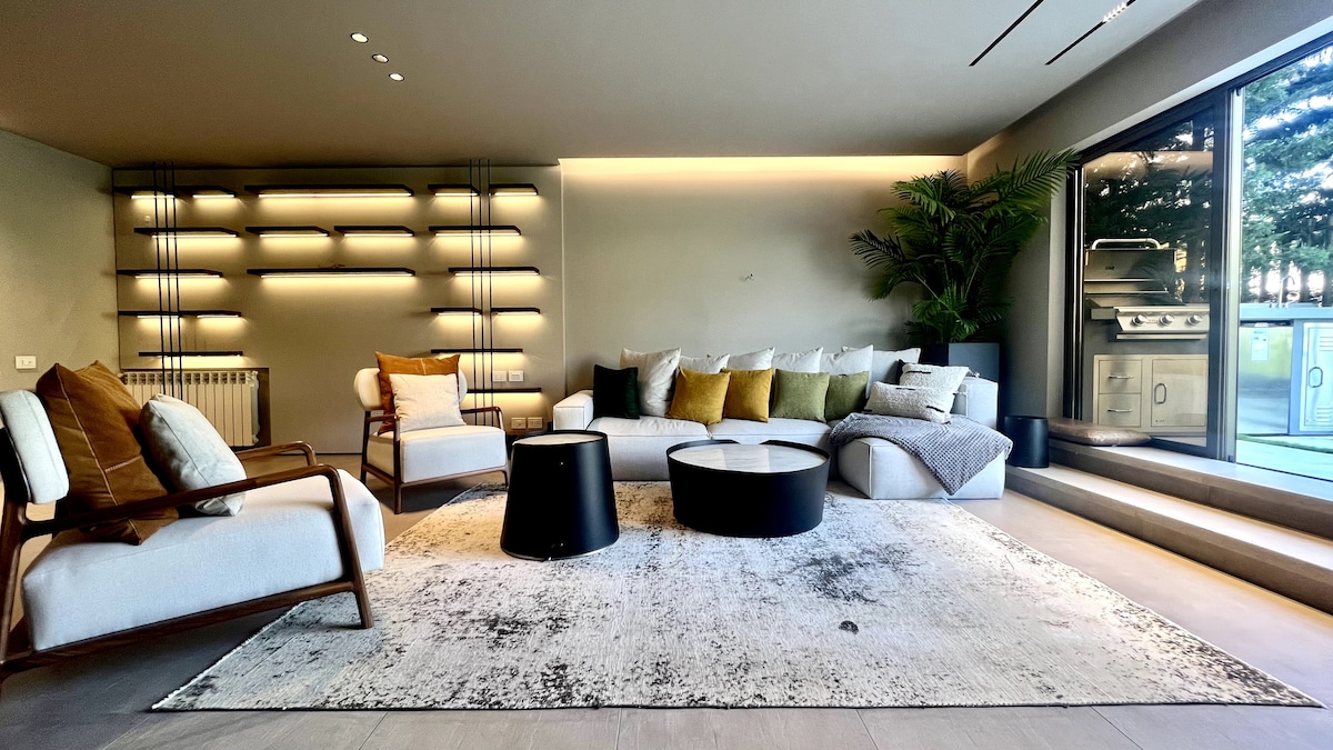 A spacious living area is highlighted by contemporary furnishings, including a sectional sofa adorned with cushions in soft hues. A coffee table sits at the center on a textured area rug. Large glass doors offer views of an outdoor terrace, enhancing natural light.
