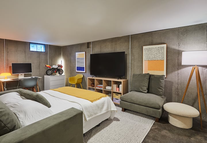 La seconda camera nel seminterrato/ufficio. Nuovissimo (2023) West Elm Sofa Bed and Ottoman in Suede performance Velvet. C'è un accogliente tappeto, un riscaldamento a pavimento radiante e un enorme monitor Samsung, insieme a una tastiera e un mouse Apple