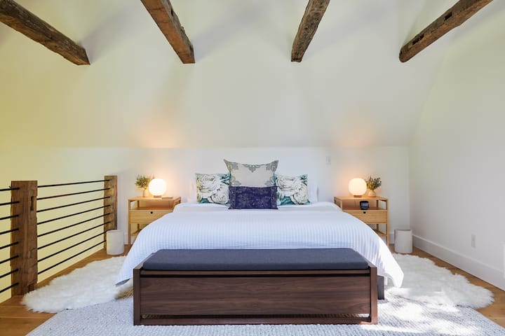 Camera da letto principale con design all'interno di panca, lampade da comodino stampate in 3D, tappeto di articoli morbidi, biancheria di lusso e tonnellate di luce naturale (nota che non ci sono tende nella casa, quindi porta una mascherina per gli occhi, se vuoi!)