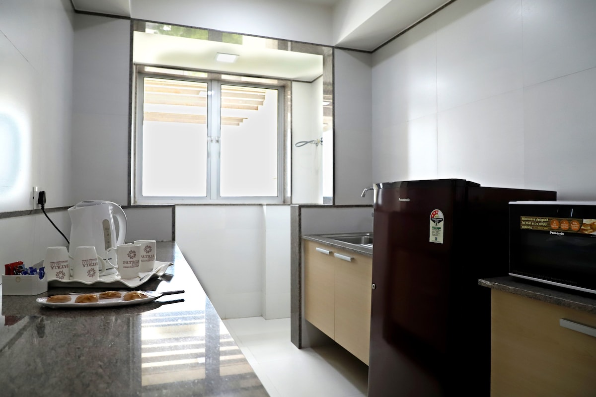 A modern kitchenette is equipped with essential appliances including a kettle and microwave. Counter space is available for meal preparation, with cabinets offering storage. A window allows natural light to fill the room, enhancing the workspace.