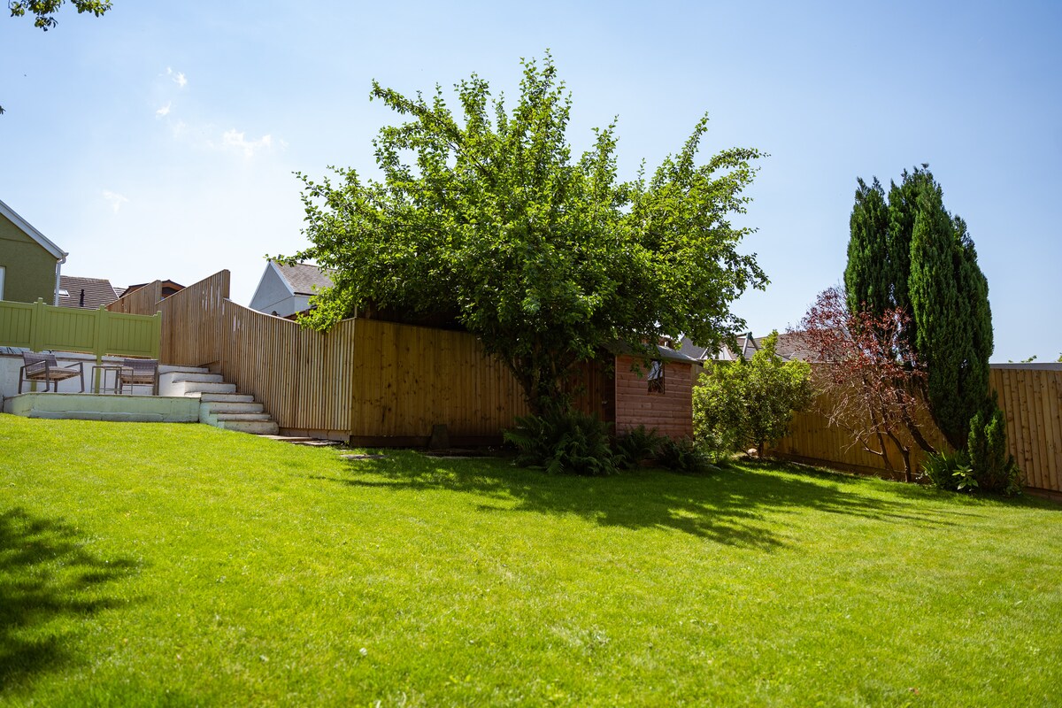 A spacious garden area is highlighted, featuring a large lawn with an apple tree and various ferns. Fenced for privacy, the garden includes two patio areas and gentle steps leading to the elevated section of the yard.