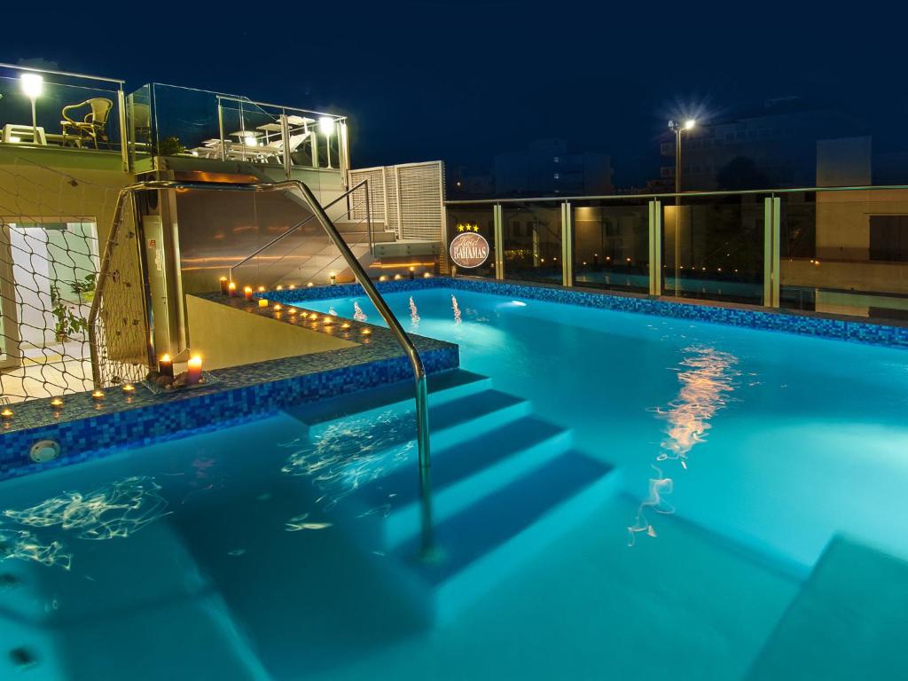 A well-lit swimming pool is framed by tiles, with shimmering water reflecting surrounding lights. Stairs lead from the pool's edge, while the area is enhanced by decorative candles that illuminate the space, creating a serene ambiance for relaxation.