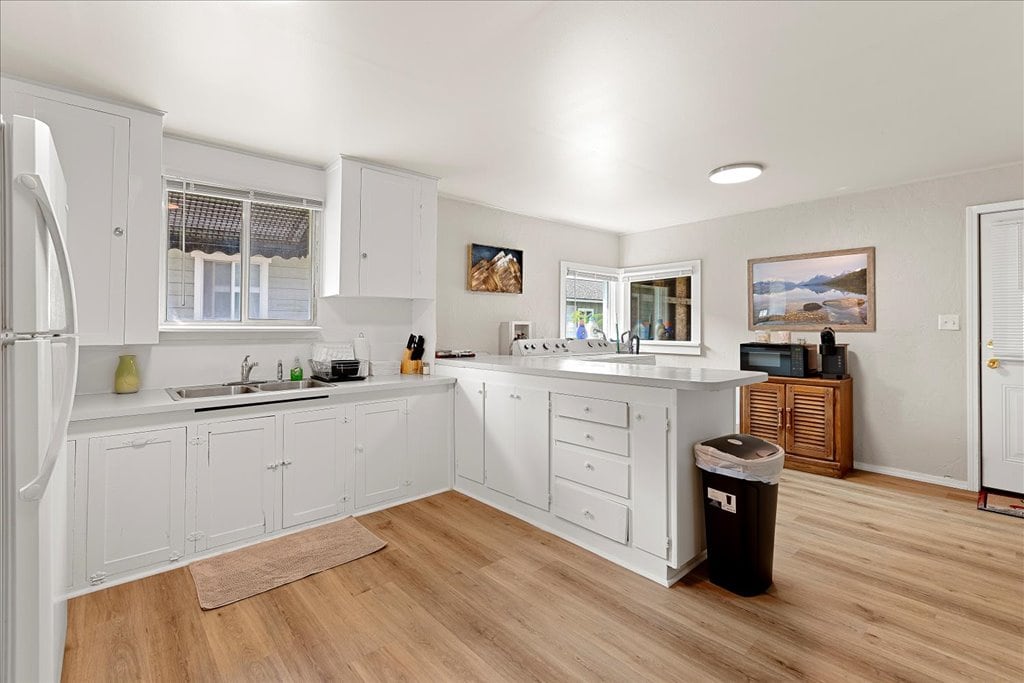 A well-appointed kitchen features white cabinetry, modern appliances, and ample counter space. Natural light enters through the window above the sink, while a calm, neutral color palette creates a spacious feel. A small rug lies on the floor, complementing the vinyl plank flooring.