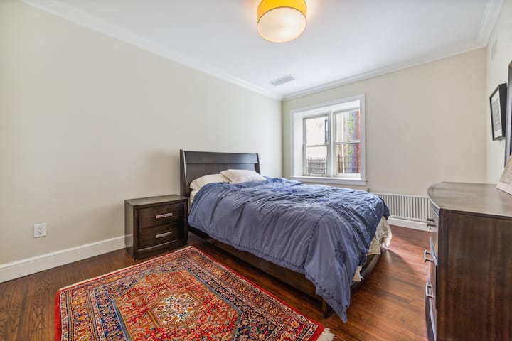 The Corner Bedroom, with a bedroom set including a queen platform bed, a low dresser with a mirror, and night tables.  U prostoriji se nalazi i veliki ormar i prozor okrenut prema jugu koji gleda prema dolje na vanjski prostor. 