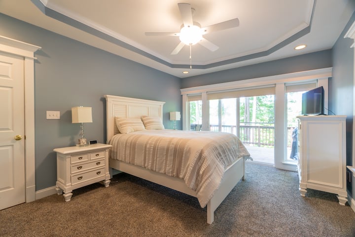 El dormitorio principal cuenta con una cómoda cama tamaño king, TV de pantalla plana, baño privado y espacio de trabajo dedicado con escritorio. Las grandes puertas corredizas de vidrio se abren hacia la terraza frente al lago con comedor al aire libre, mesa de ping-pong, hermosas vistas al lago y una vida interior y exterior perfecta
