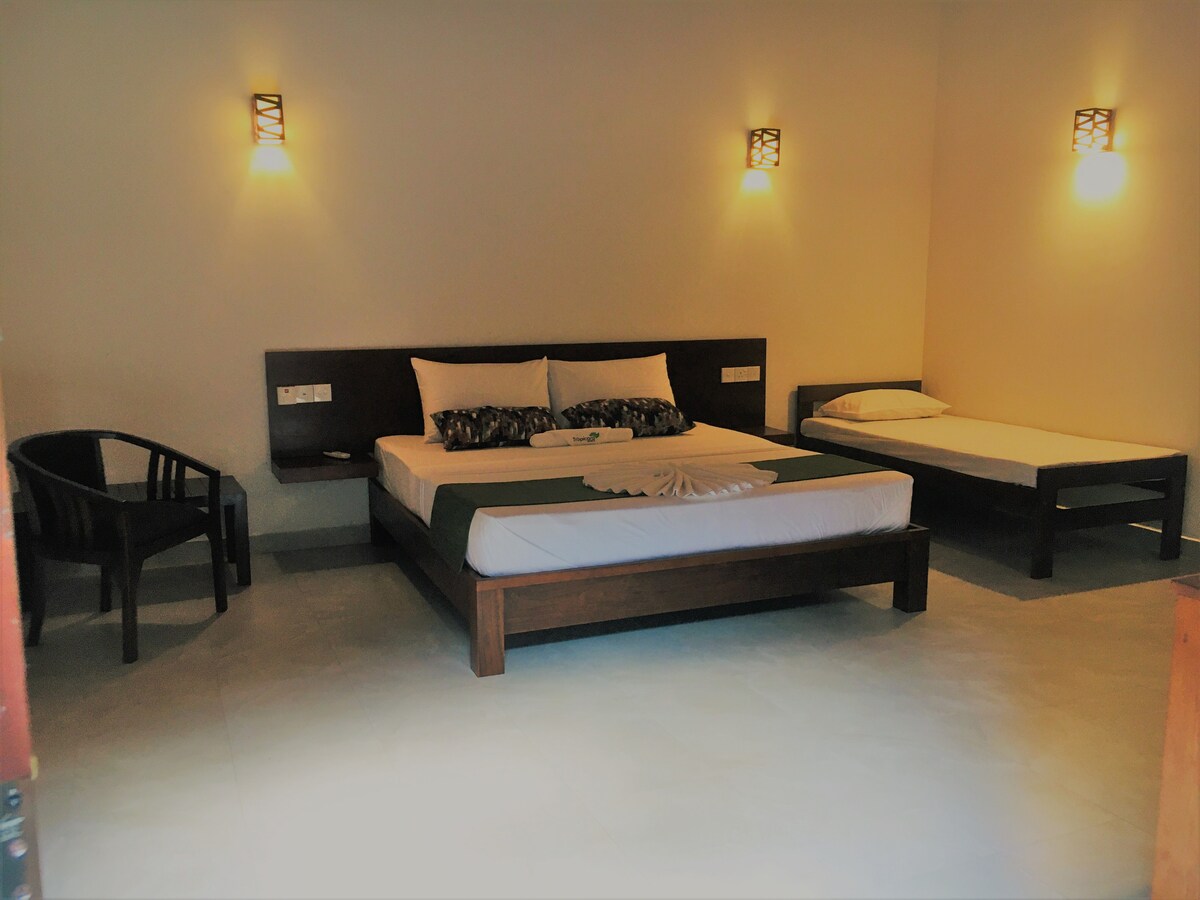 A spacious sleeping area features a large bed with decorative pillows and a smaller bed beside it. Two cozy lamps are mounted on the walls, providing soft lighting. A simple chair is set near the entrance, complementing the minimalist design.