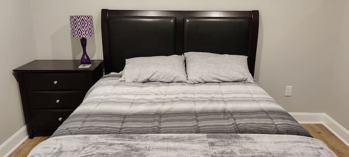 Bedroom Two has one queen sized bed, two pillows, a chest of drawers to store your clothes, a nightside table with a lamp and a closet with hangers. 