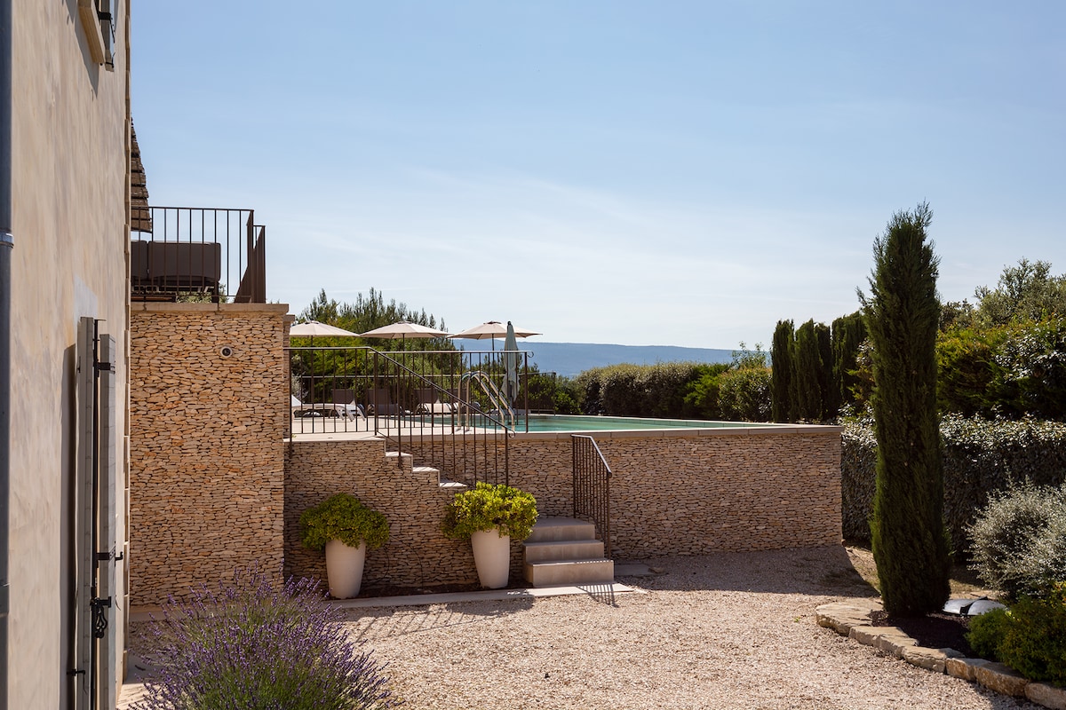 The exterior features a private swimming pool surrounded by sun loungers and umbrellas, offering a relaxing outdoor space. Step stone access leads from the villa to the pool area, framed by neatly landscaped greenery and stone walls that complement the natural aesthetic.