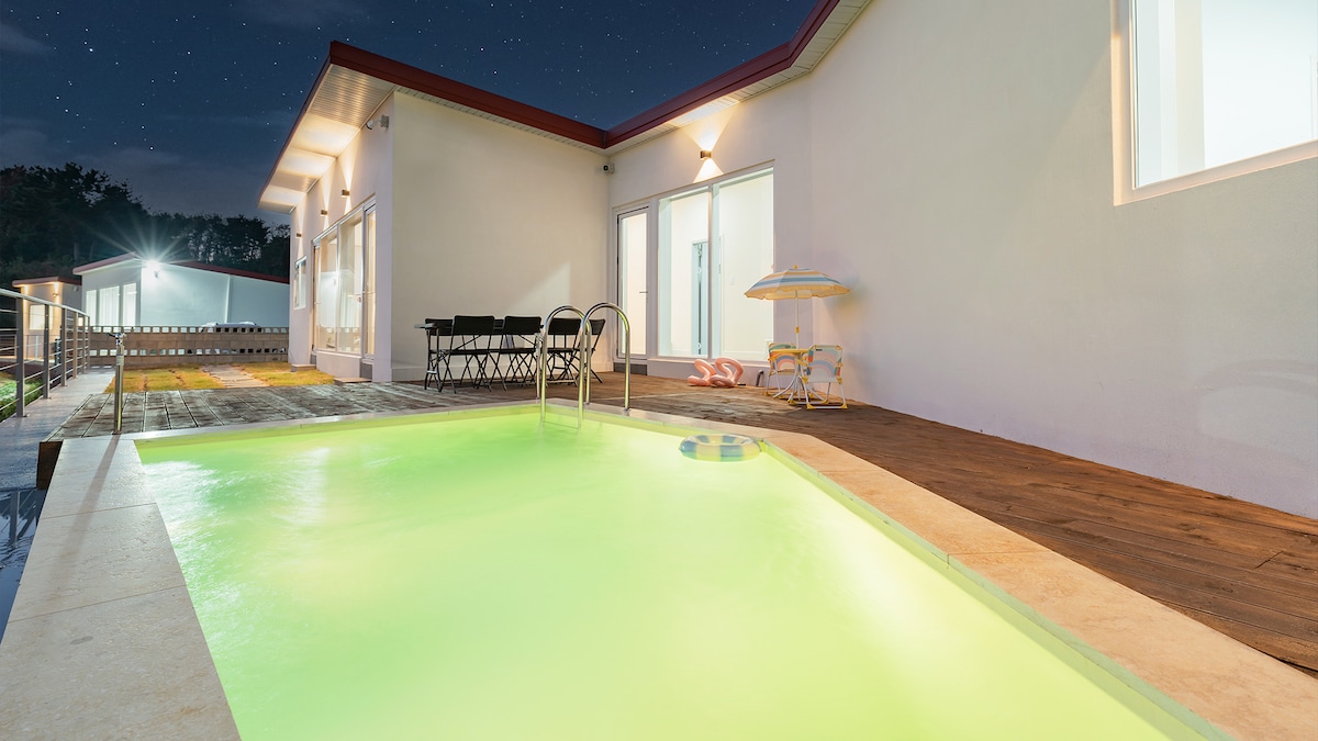 A private pool area is highlighted under a star-filled sky, featuring a softly illuminated pool. The space includes a wooden deck and a lounge chair, with a table set for outdoor dining visible in the background.