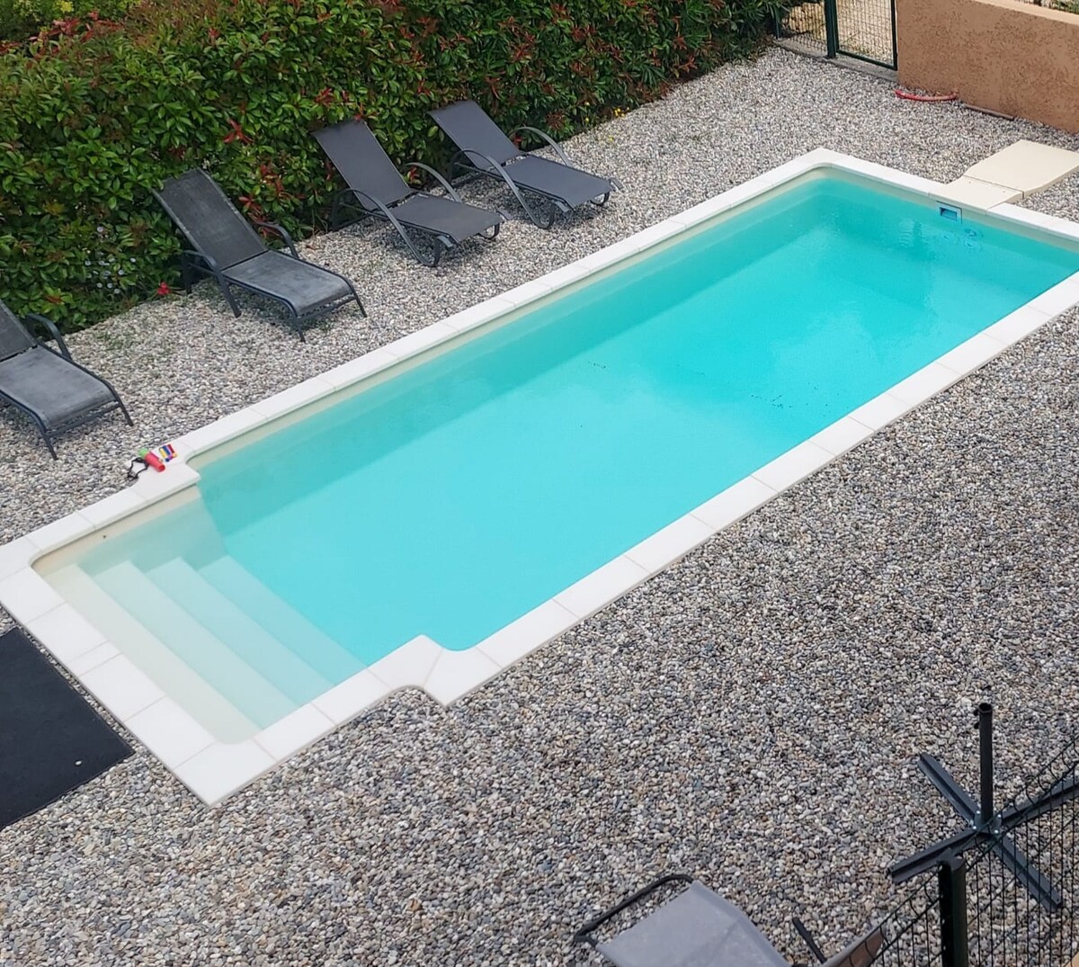 A private swimming pool is surrounded by a pebble patio, featuring several sun loungers positioned for relaxation. The pool, measuring 7m x 4m, is accessible by shallow steps. Lush greenery borders the area, providing a serene setting.