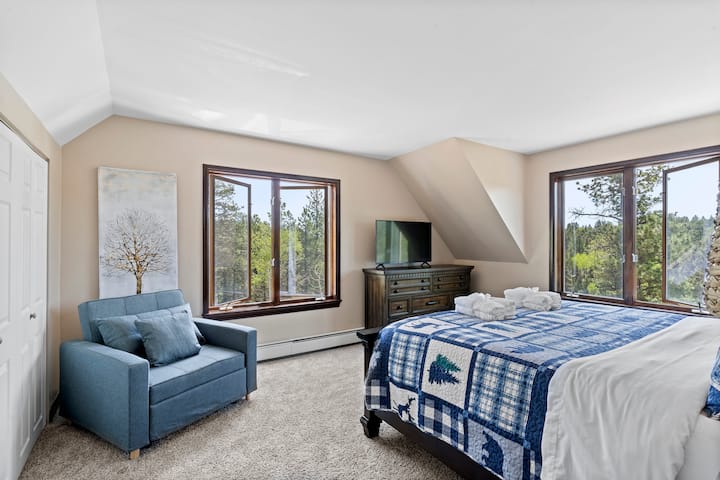 Спалня на горния етаж с голямо двойно легло и телевизор. Големи прозорци с красива гледка. 