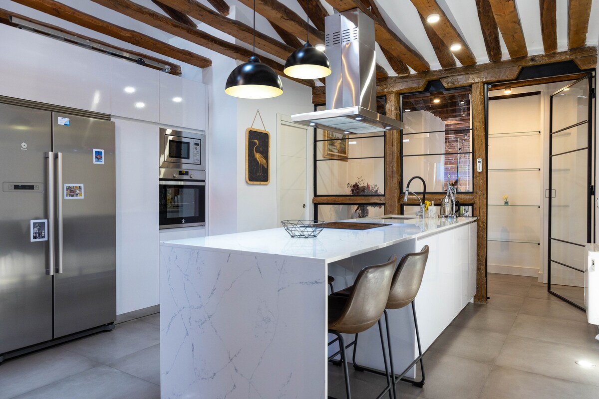 The spacious kitchen features modern appliances and a large island with seating. Exposed wooden beams highlight the ceiling, creating a warm atmosphere. Ample cabinetry and a stylish backsplash enhance the functional layout, offering ideal space for cooking and gathering.