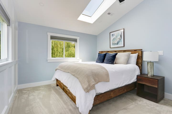 Primary bedroom featuring a skylight, king sized bed, 38inch flat screen with soundbar, and spacious walk in closet & vanity en-suite full bathroom. 
