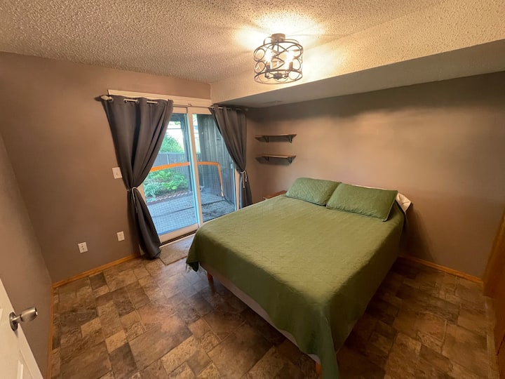 Chumba cha kulala cha ghorofa na kitanda cha malkia kilicho na ufikiaji wa ngazi ya chini ya baraza na mapazia meusi. 