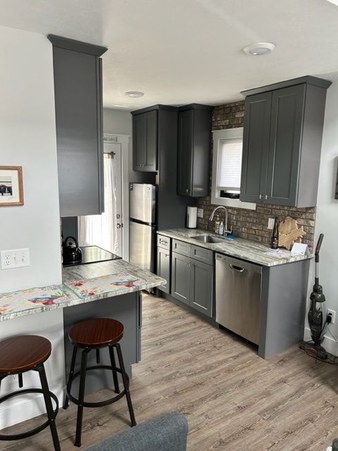 The modern kitchen features dark cabinetry complemented by a stylish backsplash. A stainless steel refrigerator and dishwasher are visible, alongside a sink and ample counter space. Two wooden barstools are placed at a small counter, enhancing the cozy dining area.
