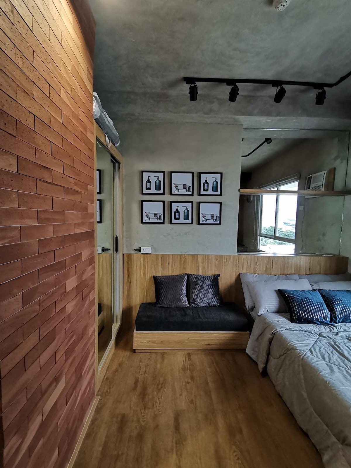 A modern interior showcases a cozy sleeping area featuring a spacious bed with neutral bedding. A comfortable sofa is positioned beside the bed, with decorative pillows arranged thoughtfully. Framed artwork adorns the wall, and natural light streams in through a window, enhancing the room's relaxed environment.