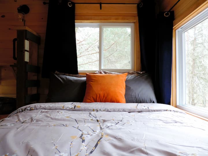 Blackout curtains frame the windows, offering views of the surrounding forest and filling the space with natural light
 