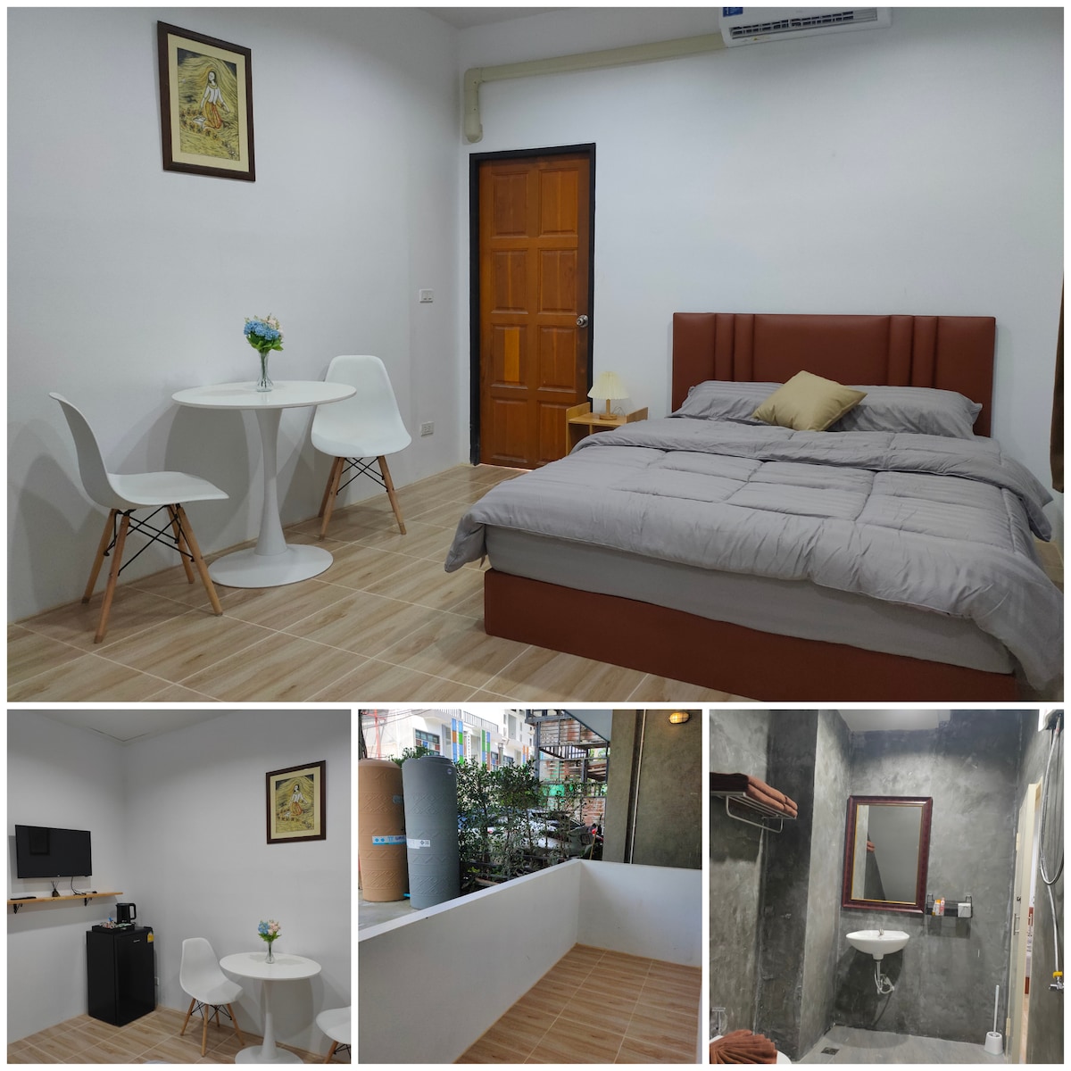 A cozy guest room features a spacious bed with a neutral-toned duvet and a decorative pillow. A small dining table with two chairs is positioned beside the bed. A kitchenette area includes essential appliances, while a private balcony offers a view of the surroundings.