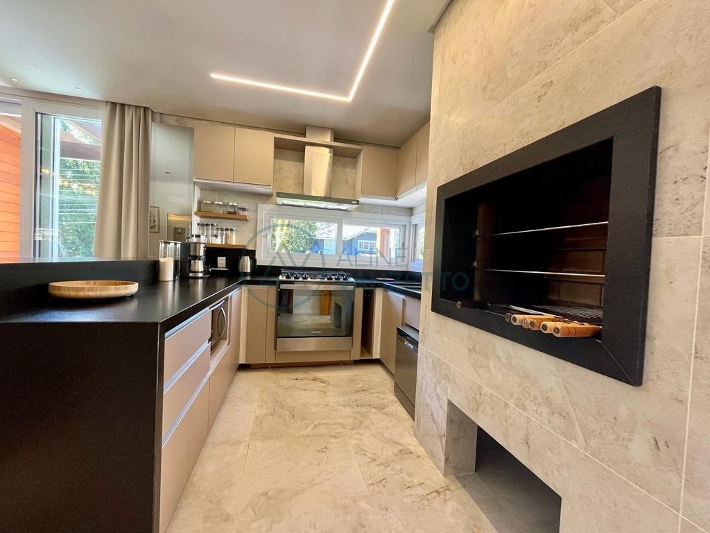 A modern kitchen is shown with sleek cabinetry and a black countertop. Stainless steel appliances, including a gas stove and oven, are included. A built-in fireplace is visible, adding a functional design element. Natural light enters through large windows, illuminating the space.