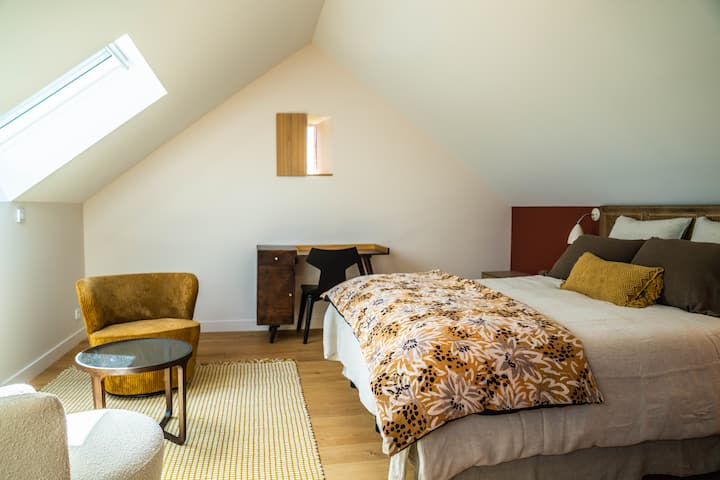 تحتوي غرفة النوم الثانية في الطابق العلوي، المغمورة بألوان هادئة، على منطقة مكتب ومنطقة جلوس لجو مريح.