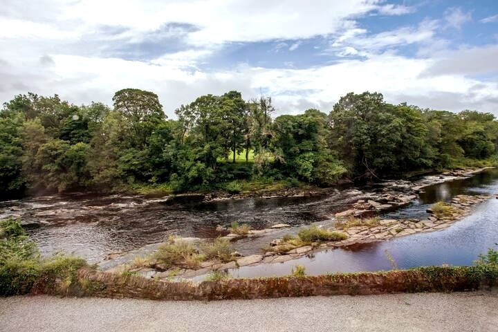 The serene River Tees flows gently past, bordered by lush greenery and rocky banks. This peaceful view captures the natural landscape and tranquility of the area, inviting moments of reflection and connection with nature.