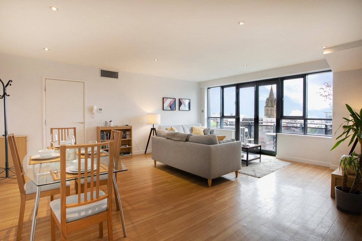 An open living area features large windows allowing natural light to fill the space. A comfortable sofa is complemented by a coffee table, while a dining table with chairs is set nearby. Subtle decorative accents and a potted plant add warmth to the modern design.