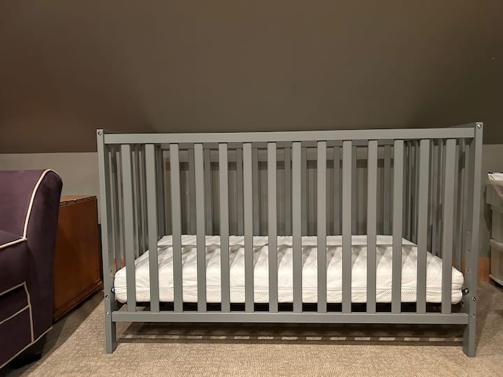 Standard size permanent crib with sheets off the main kid's bedroom
