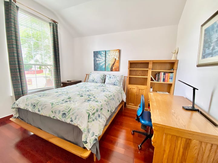 クイーンサイズベッド、テーブル、椅子、本棚、素敵な装飾、大きな窓を備えた最初のベッドルームです。