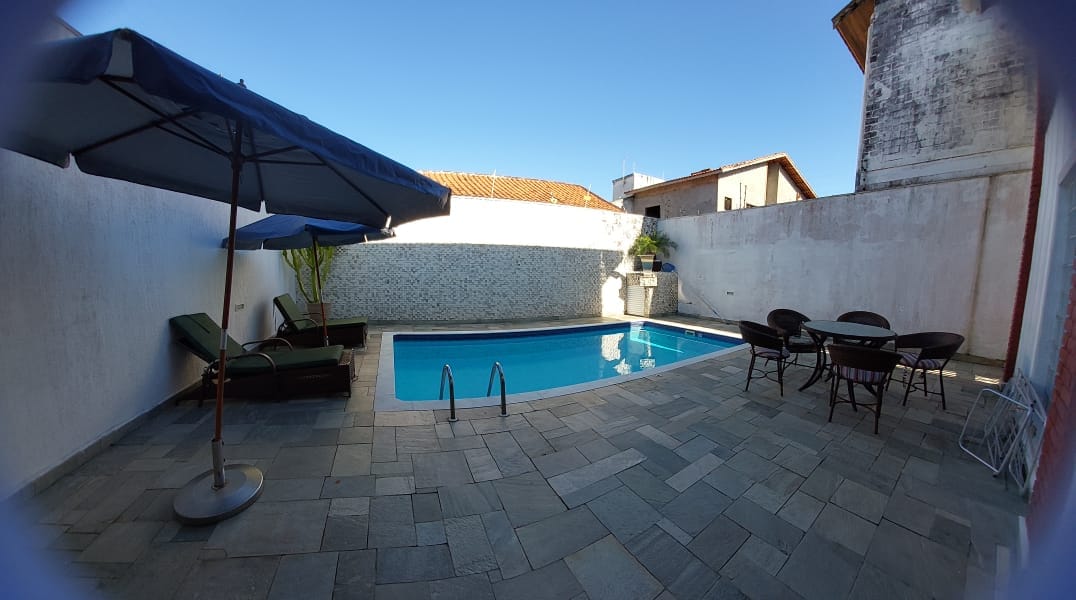 A private pool area is provided with a clear blue pool surrounded by paved stone flooring. Comfortable loungers sit beneath a large umbrella, and a dining table with chairs is positioned nearby. Lush greenery is visible beside the pool, enhancing the serene environment.