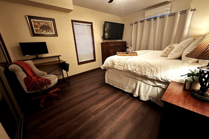 غرفة نوم أساسية في الطابق السفلي مع سرير بمقاس كبير ومساحة عمل مخصصة.