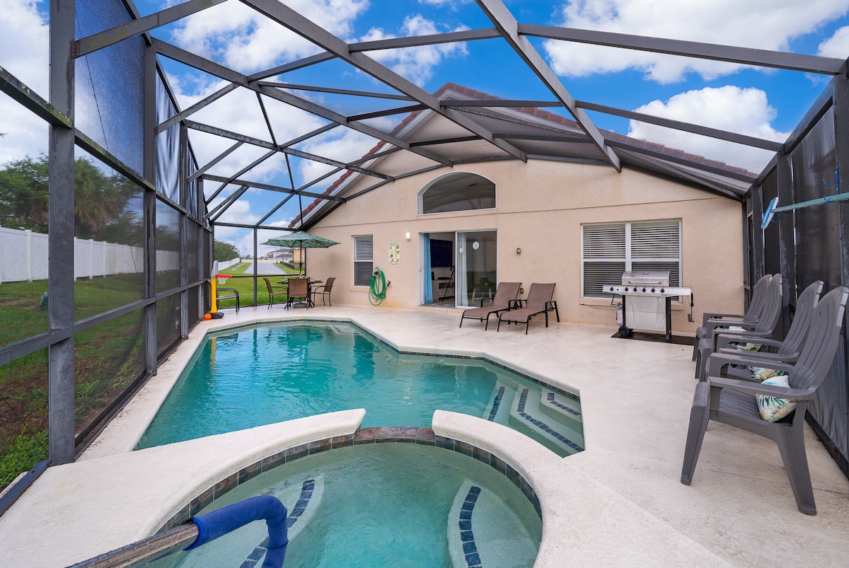 A private pool area features a turquoise swimming pool and a spa, both enclosed by a screened lanai. Comfortable seating options include several lounge chairs and a propane grill is available nearby, creating an inviting space for relaxation and outdoor dining.