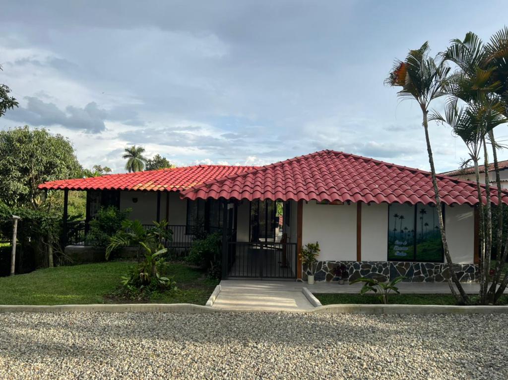 A charming chalet with a red tiled roof is surrounded by lush greenery. The entrance is paved and features a gravel driveway. Large windows allow natural light to fill the interior, while tropical plants add a touch of nature to the exterior.