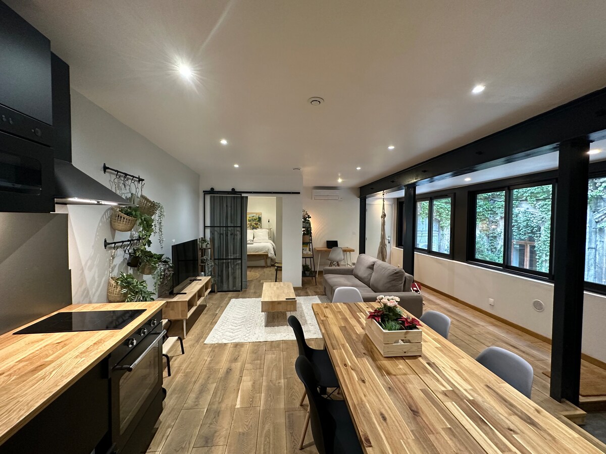 A spacious open-plan living area is showcased, featuring a dining table surrounded by chairs. Natural light enters through large windows, illuminating the wooden flooring. A kitchen area is equipped with modern appliances, while a comfortable sofa and a stylish coffee table offer a cozy seating option.