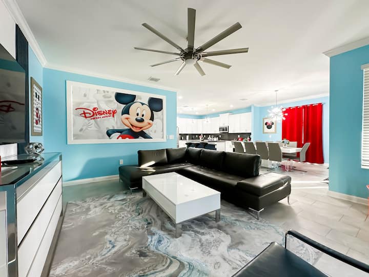 Zakoračite u ovaj vedri dnevni boravak i blagovaonicu otvorenog plana! Zidovi u svijetloplavoj boji i crvene zavjese stvaraju razigranu atmosferu u stilu Disneyja, a tu su i sjajne crne garniture, moderni bijeli stolić za kavu, ukrasi s likom Mickeyja i ugodna blagovaonica za cijelu obitelj.  