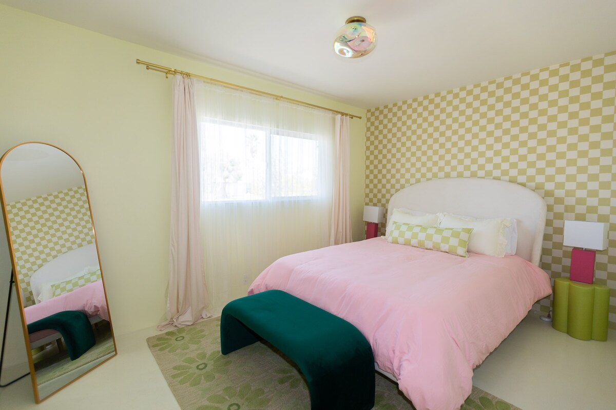 تتميز غرفة النوم الخضراء بورق حائط Spoonflower الممتع، وخزانة كاملة، ومرآة كاملة الطول، وإضاءة علوية ناعمة. 