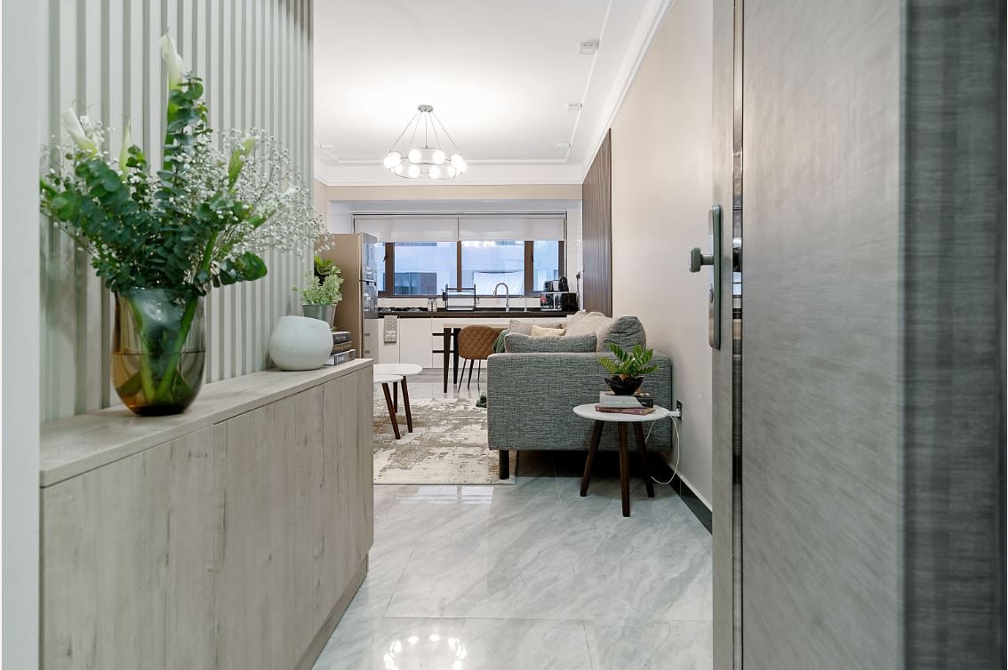 A welcoming entrance showcases a decorative console table adorned with greenery and thoughtful accents. The open layout reveals a spacious living area in the background, with modern furnishings and abundant natural light filtering through large windows.