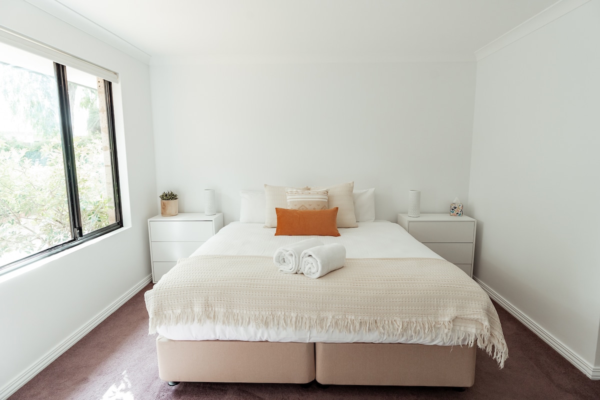 这间宽敞的卧室设有一张豪华加大双人床，配有毛绒床上用品、带现代灯具的床头柜、自然采光的大窗户和温馨的装饰，营造宁静轻松的氛围。