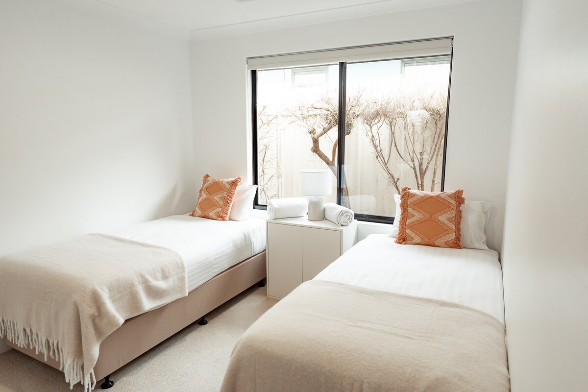 这间明亮的卧室设有两张舒适的单人床，配有柔软的床上用品和装饰性靠垫，一张共用床头柜，上面摆放着干净的毛巾，还有一扇大窗户，自然光线充足，可欣赏私人庭院的美景。