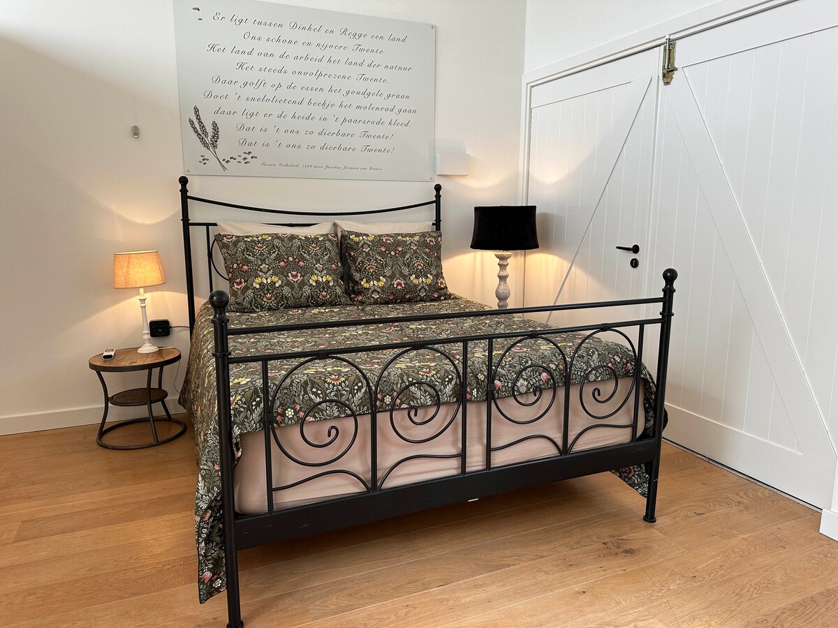 Kráľovská posteľ v priestore na spanie s veľkými dverami stodoly, ktoré môžu byť otvorené, keď nie sme doma.