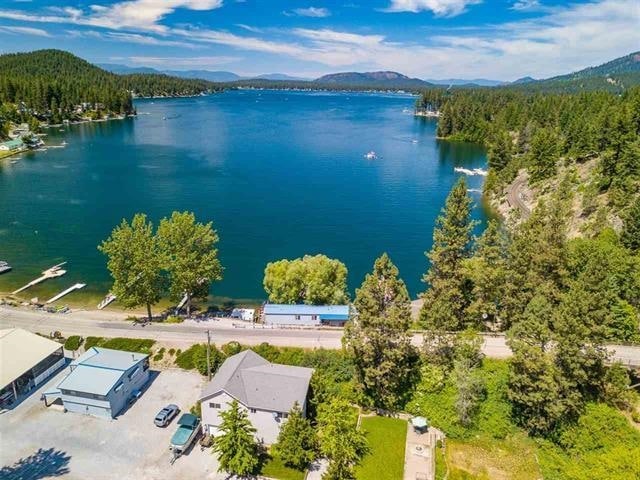 An aerial view showcases the Lake House and its proximity to Loon Lake. The blue water reflects the sky, with boats visible on the surface. Lush greenery lines the shore, and nearby residences are nestled among the trees, creating a serene, natural environment.