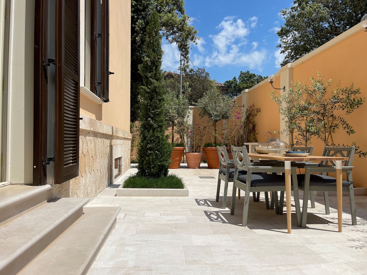 The private garden features a spacious patio area adorned with greenery and decorative potted plants. A dining table with chairs is positioned for outdoor meals, while the surrounding space offers a serene atmosphere under a clear blue sky.