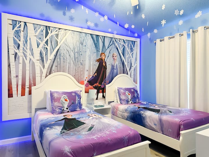 ห้องนอนธีม Frozen ที่เต็มไปด้วยความมหัศจรรย์สำหรับเจ้าหญิงตัวน้อย! มีเตียงแฝด 2 เตียง โต๊ะข้างเตียงแบบใช้ร่วมกัน พัดลมเพดาน โคมไฟ ตู้เสื้อผ้า และสมาร์ททีวี ผนังสีฟ้าน้ำแข็ง รูปสติกเกอร์เกล็ดหิมะ และภาพวาดฝาผนังอาร์เอนเดลที่งดงามช่วยเติมเต็มความงดงามของที่พัก