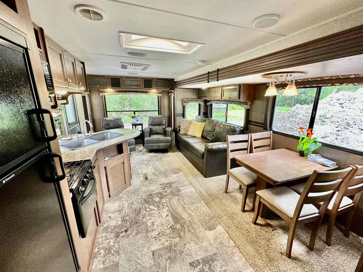 A spacious living area is presented with a comfortable sofa and two swivel chairs, positioned near windows that allow natural light. A dining table for four and a kitchen area with modern appliances are also visible, enhancing the inviting ambiance.